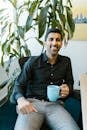 Cheerful man with coffee mug sitting in modern office with plant.